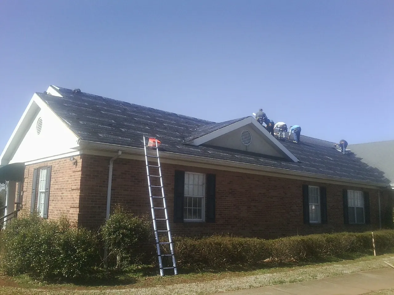 Crew tearing shingles off a brick ranch roof with a ladder set — Emergency Roof Repair work by our crew in Oak Grove
