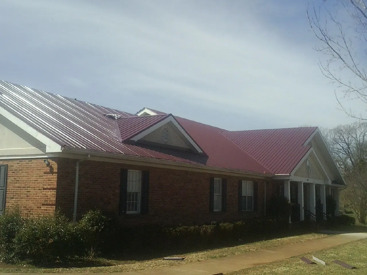 Red metal roof with gabled entries on a long brick building, from a Hail Damage Roof Repair job in Oak Grove