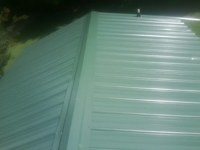 New green metal panels meeting at the ridge of a roof — Flat Roof Repair work by our crew in Oak Grove