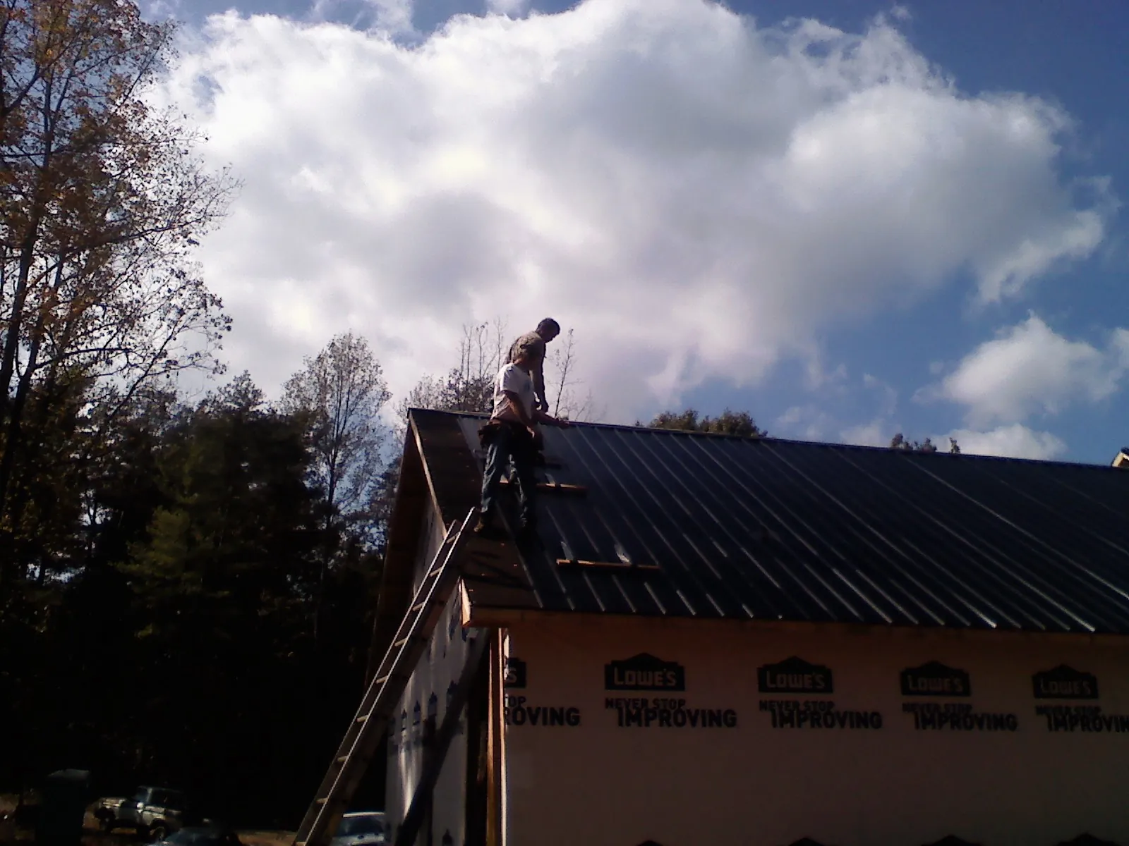 Roofer fastening dark metal panels high against a cloudy sky, from a Roof Inspection job in Oak Grove